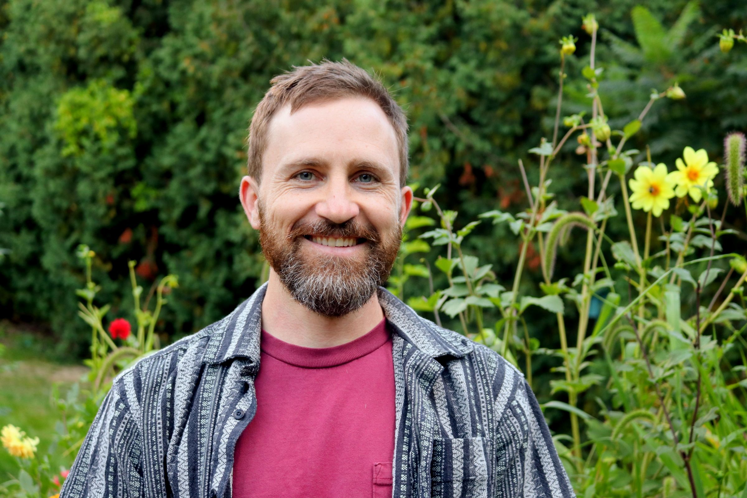 Derek Roguski smiling in an outdoor setting with wildflowers in the background. 