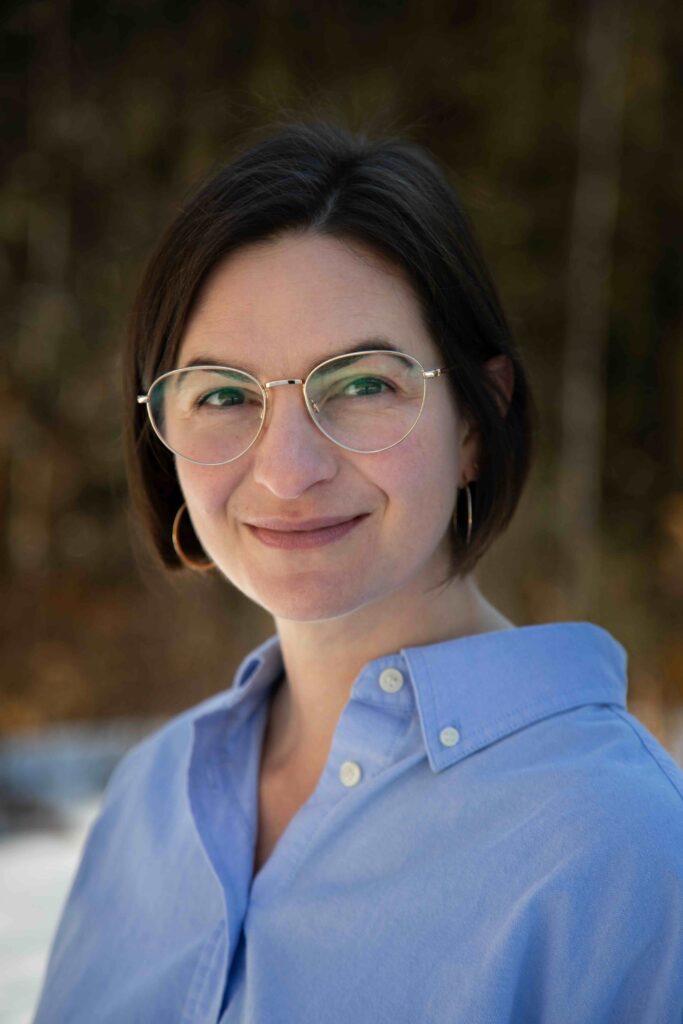 Jessica Benko. Headshot looking into camera, wearing gold rimmed glasses and a blue button down shirt